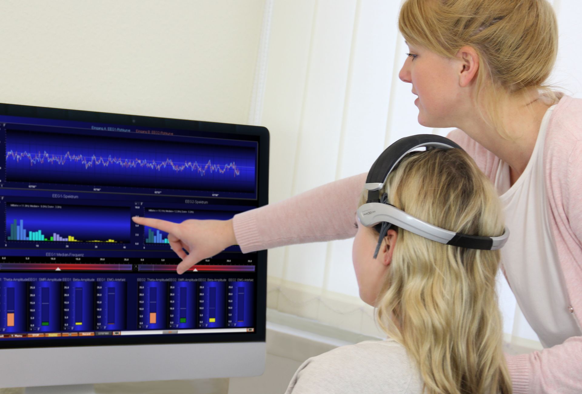 Neurofeedback-sessie: coach wijst op EEG-grafieken terwijl deelnemer een headset draagt
